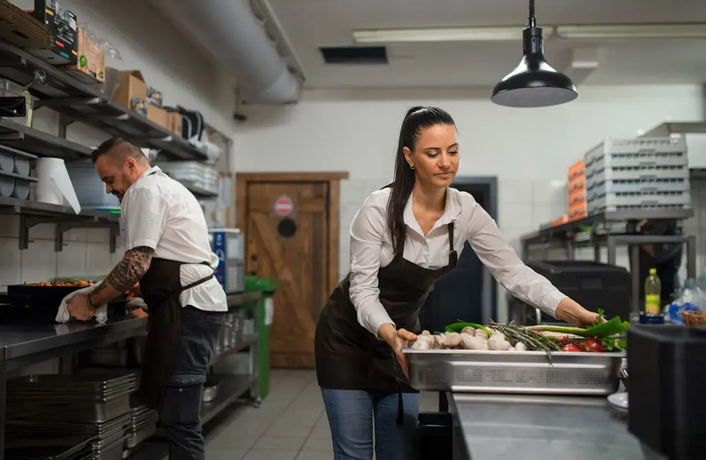 Chef and cook working on their dishes indoors in restaurant kitchen wearing fresh uniforms