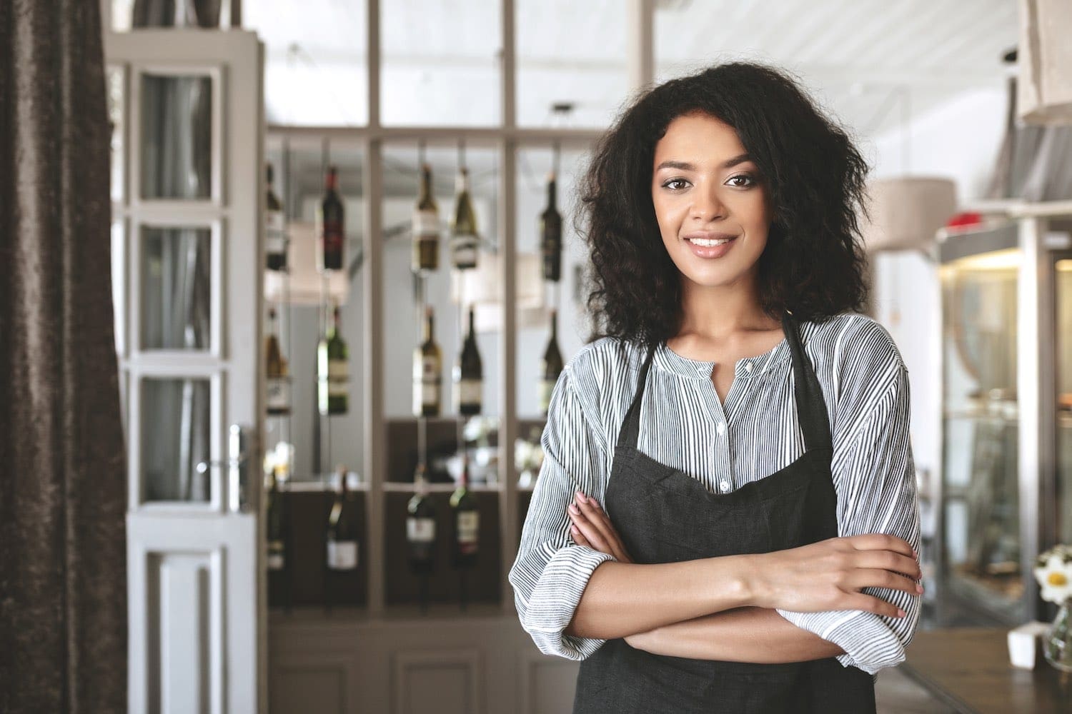 Woman wearing uniform apron with wine bottles in background